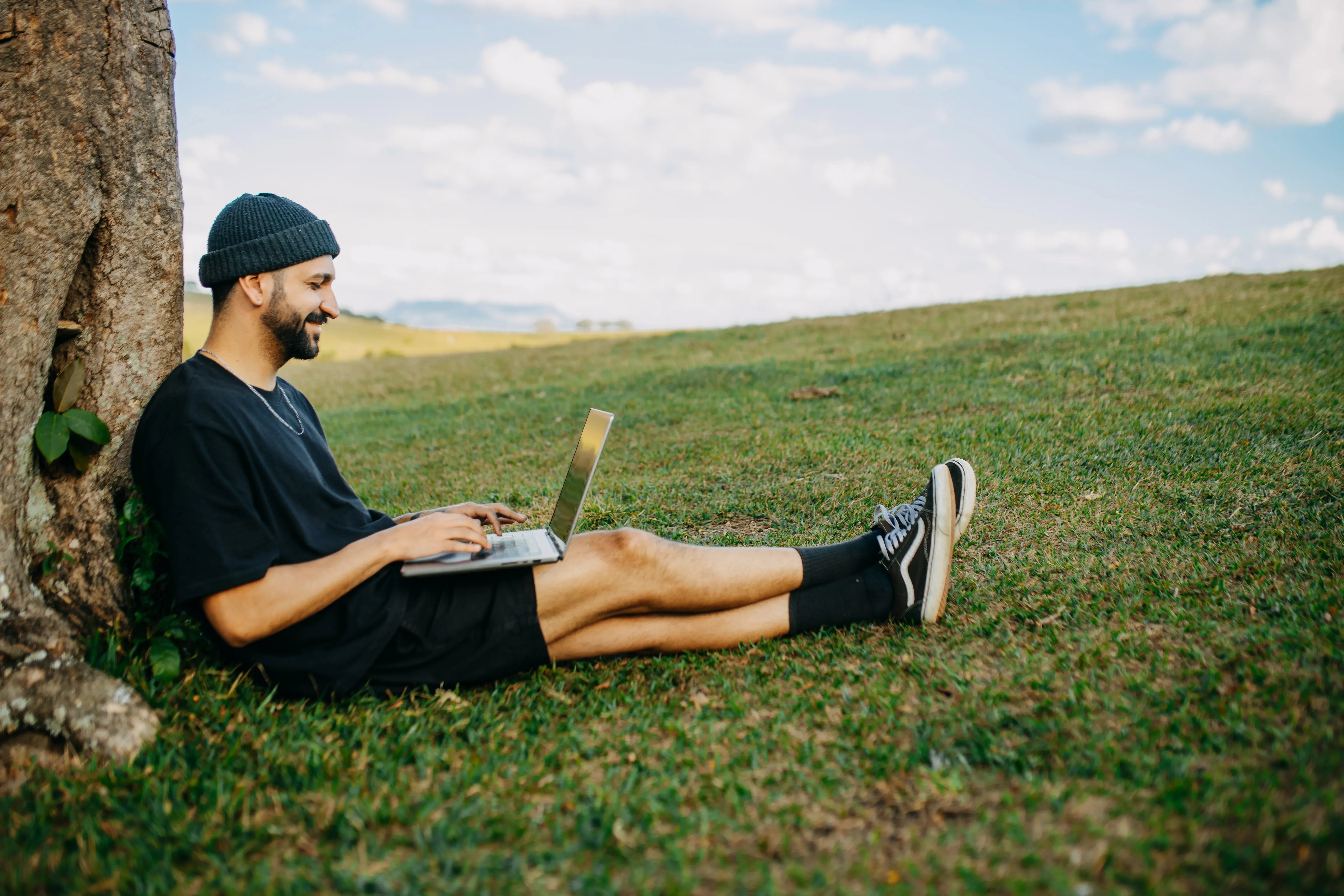 Mann sitzt mit Laptop im Gruenen und arbeitet im Freien