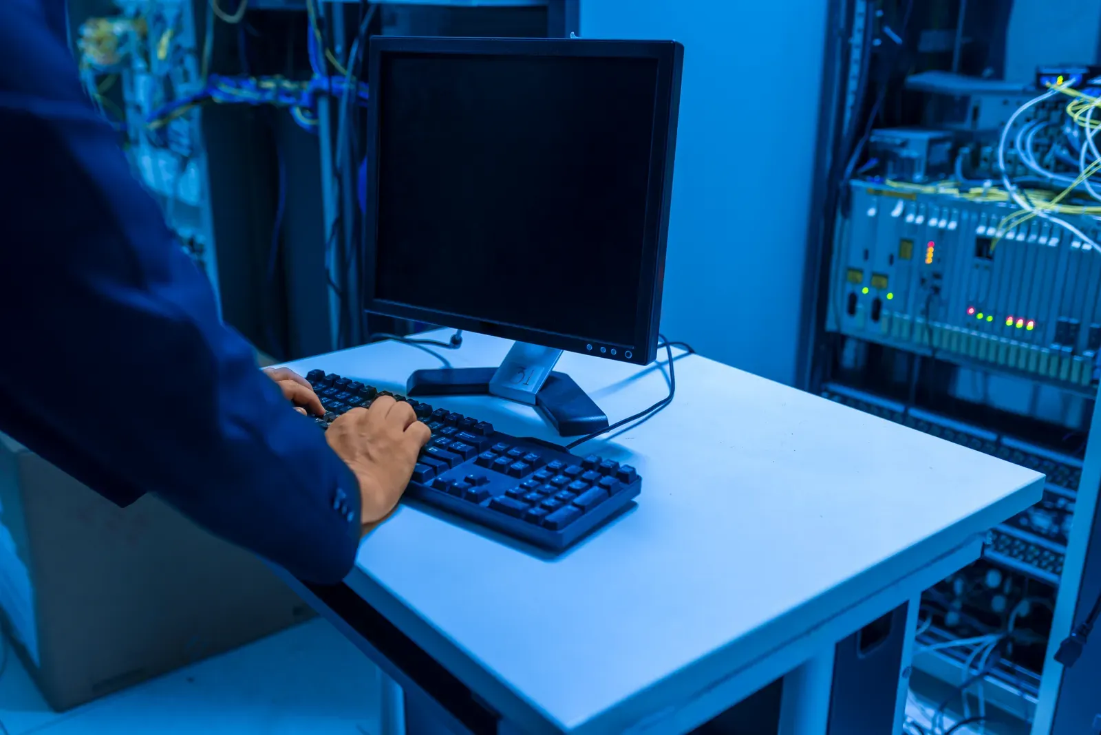 IT-Fachkraft mit Tablet und Monitor in einem Serverraum zwischen Netzwerk- und Servertechnik