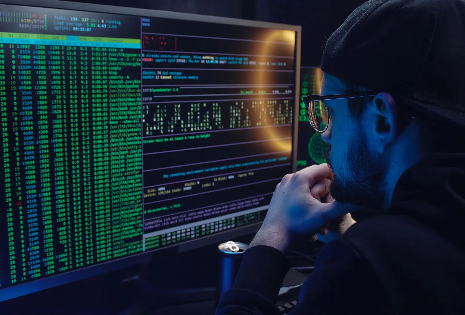 IT-Fachkraft arbeitet vor mehreren Monitoren mit Code und Sicherheitsanzeigen