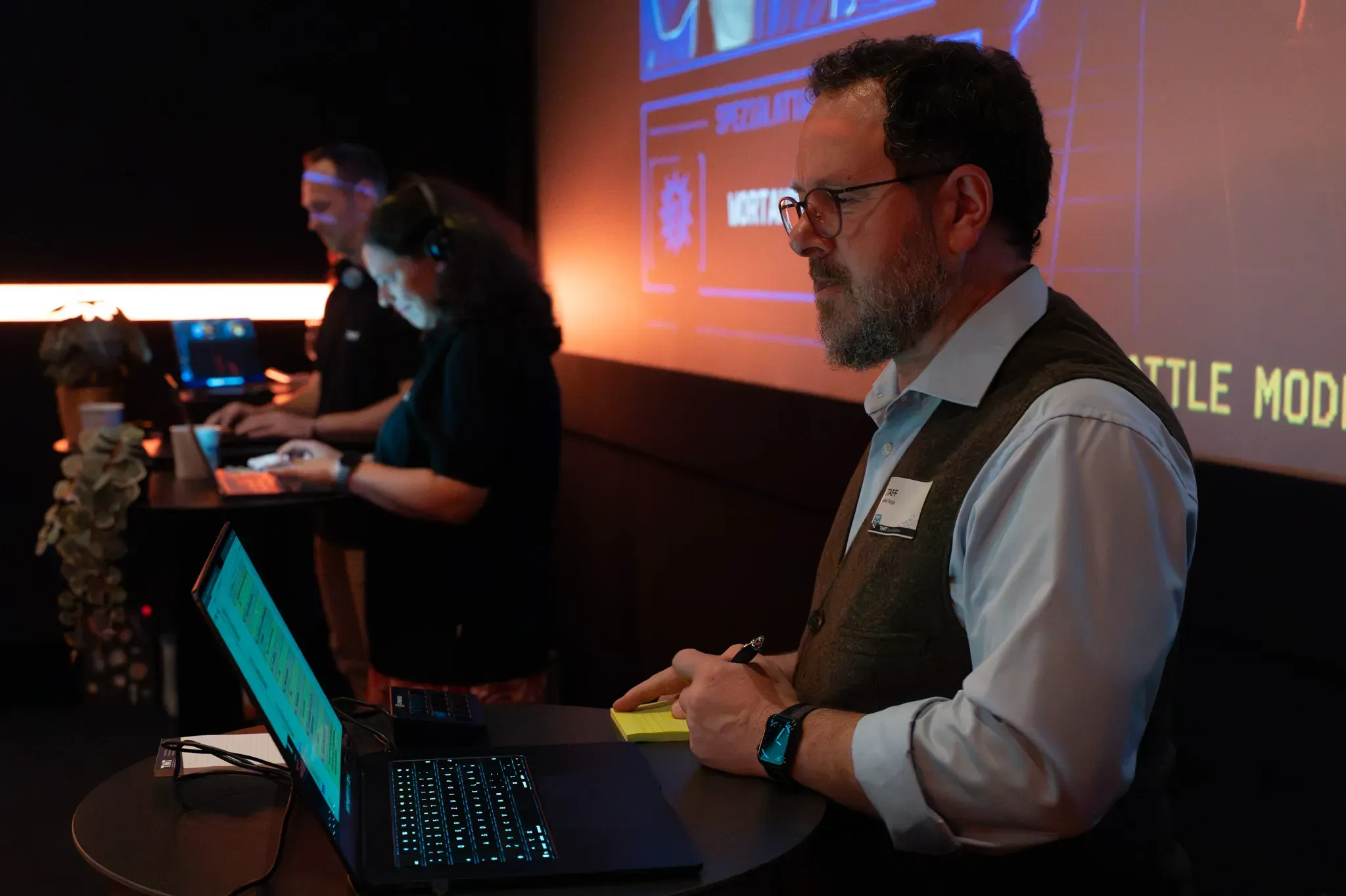 TMT-Mitarbeiter mit „Staff“-Schild am Laptop vor einer beleuchteten Leinwand