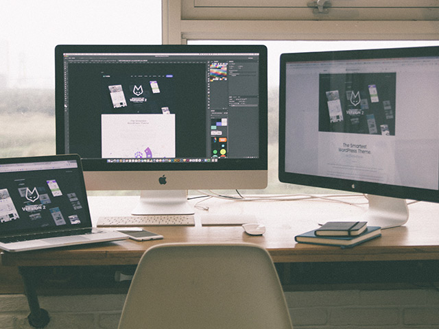 Schreibtisch vor Fenster mit Macbook, iMac und Monitor